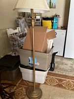 Full view of the metal standing floor lamp showing the round base, metal pole, and beige fabric lampshade.