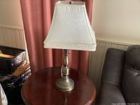 Full view of the table lamp showing the metal base and white fabric rectangular shade, placed on a round wooden table.