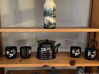 Photo of a blue Japanese style tea set including one teapot with bamboo handle and four tea cups decorated with white flowers.