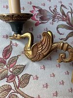 Close-up photo showing brass swan holding candle holder with intricate detail and patina.