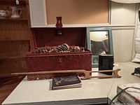 Photo showing red stepped painted wooden box filled with pine cones, wooden yarn tool, 1915 North American animal guide book, embossed leather case, and blue-green framed mirror on table.