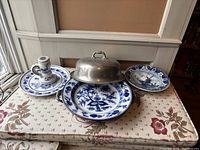 Wide view of all four items on a floral-patterned tablecloth, showing the blue and white ceramics and the pewter warming plate with lid.