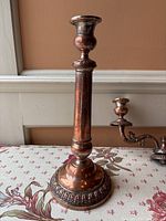Photo of single copper candlestick showing ornate round base and tall slim body with candle holder