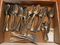 Overhead view of assorted large pewter spoons, five teaspoons and four forks laid out in a cardboard box.