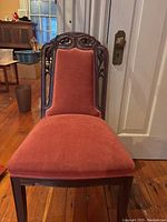 Front view of chair showing rust velvet upholstered seat and backrest with carved wood frame