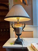 Full view of Art Nouveau style lamp with bronze base, two swan arms, and pleated beige cloth shade.