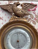 Front view of the vintage barometer showing circular face with weather predictions and perched eagle figure on top.