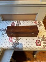 Closed wooden rectangular box on floral surface.