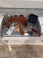 Leather key chains, wallets, metal keychain, and wristband arranged on a steel tray