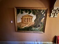 Wide angle photo showing the full framed painting hanging on a wall. Shows Greek temple with tree composition.