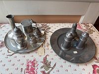 Overview of two pewter trays with assorted small decorative and functional pewter items arranged on a floral cloth.