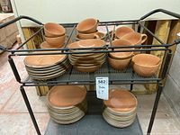 Three-tier metal rack holding nested mugs, saucers, bowls and plates