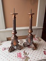 Pair of large antique copper candlesticks on floral fabric background, showing full height and design