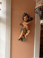 Cherub playing violin sculpture, showing detailed facial features, green cloth draping, and violin in hands.