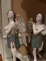 Front view of both plaster angel statues side by side, showing wings, draped skirts, and bases.