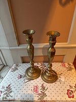 Pair of brass candlesticks displayed on floral fabric against a wall showing their size and shape.