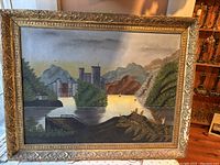 First painting, large landscape showing a castle by water with mountains and trees. Frame with ornate design, canvas has a visible tear or damage as depicted in close-up image lstimg_01jhxm5mkweh19qfhx1kxxbhca.
