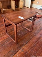 Angular view showing the teak wood end table on a wooden floor with visible repairs and wear on the legs and surface.