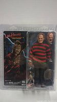 Full packaging of Freddy Krueger action figure with movie artwork, visible figure, alternate head, claw glove, and hat inside clear plastic box.