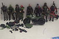 Front view of 8 G.I. Joe Classified Series action figures lined up with motorcycle and assorted accessories including weapons and armor pieces