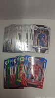 Multiple soccer trading cards laid out on a surface, showing players from various clubs such as Chelsea, Liverpool, and others, with some holographic cards visible.