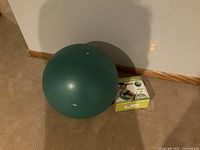 Round green balance ball placed on carpet near wall with original box beside it.