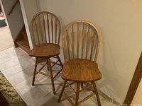 Two oak bar stools positioned next to a wall and near stairs, showing full front and side views.