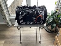 Image of a black and white zebra-striped soft cat carrier placed on a small table with a cat wand toy attached to it.