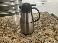 Photo of Gevalia stainless steel coffee carafe with black handle and lid on kitchen countertop.