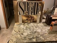 Crystal cake platter displayed on kitchen counter next to its original box with 'Sheila' branding.