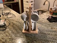 Photo of three white ceramic cups and four matching saucers displayed on a natural wood vertical stand on kitchen counter.