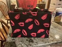 Front view of black Kate Spade tote bag with red lips print and black handles.