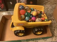 Yellow Little Tikes toy dump truck with multiple colorful balls inside on cardboard surface.