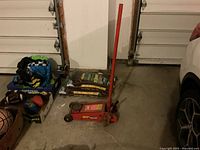 Photo showing a red MVP Super Lift floor jack used for automotive work, placed on a concrete floor in a garage.