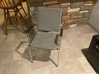 Front and angled view of office chair showing gray fabric seat and back, chrome metal legs, and black armrests.