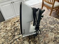 Side view of the white and green Proctor-Silex iron resting on a granite countertop showing the soleplate and wrapped power cord.