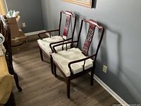 Pair of rosewood chairs with white cushions, arranged side by side on a wood floor against a gray wall.