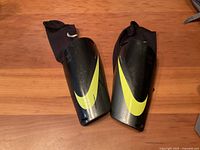Photo of a pair of black Nike soccer shin guards with yellow swoosh logos, each accompanied by a black Nike elastic sleeve with drawstring.
