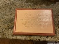 Photo of a rectangular wooden plaque with an engraved inspirational quote about success, framed with a thin dark wood border, good condition with visible light wear.