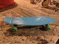 Toy skateboard on carpet with blue textured deck and green wheels