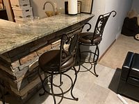 Two stools positioned at a kitchen island with granite countertop and stone facade base