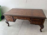 Front view of wooden executive desk showing carved legs, four drawers with metal handles, and decorative top surface.