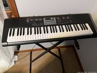 Front view of black Casio electronic keyboard piano on metal adjustable stand in a corner of a room.