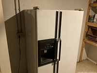 Front view of white Kenmore side-by-side refrigerator with black ice and water dispenser section on freezer door. Unit appears to be in a basement or storage room setting.