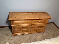 Front view of the wooden dresser showing six drawers with round knobs and wood grain finish.