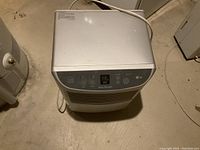 Front top view of white LG humidifier showing control panel and power cord on concrete floor.