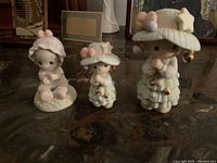 Front view of three Precious Moments porcelain statues arranged by size on a glass surface