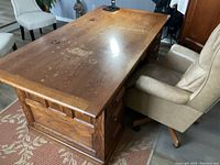 Top view of solid wood desk showing flat surface with wood grain and wear marks, accompanied by a beige office chair.