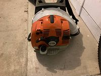 Front view of blower engine housing showing orange intake cover and white blower body