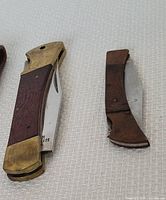 Two vintage pocket cutters on a white textured background, showing wooden handles with brass bolsters and steel blades, one larger and one smaller.